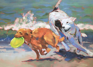 Two dogs running on the beach with a frisbee in their mouth.